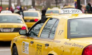 Line of Union Cabs at a protest. A driver is holding a raised fist out of their window.