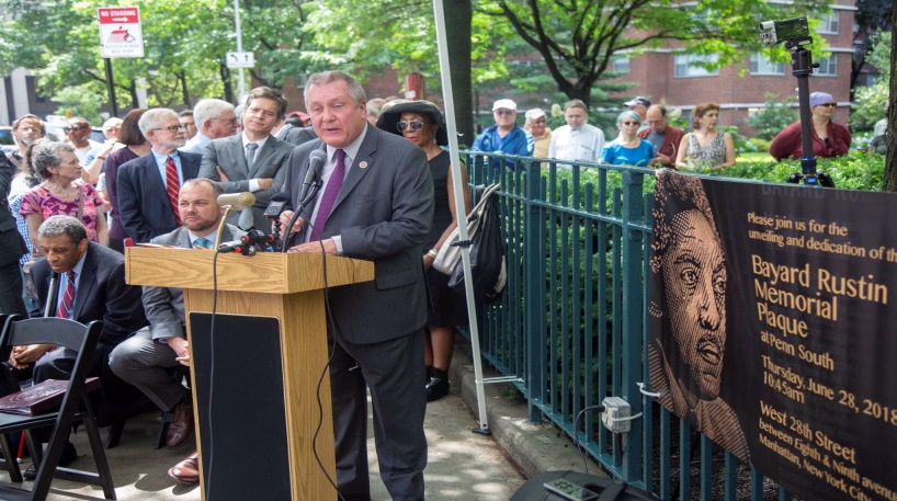 The 2018 unveiling of the Bayard Rustin plaque at Penn South Co-op. Norman Hill sits to the left of the speaker and Velma Hill is standing to the right of the speaker. The honor was a long time in coming.